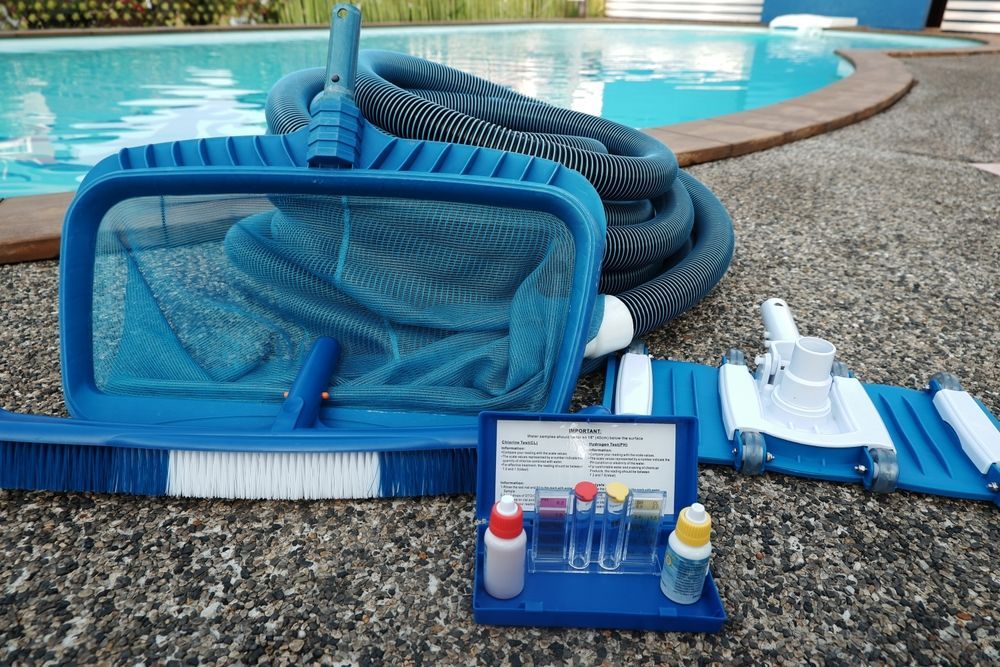 A Pool Cleaning Supplies: Net, Brush, Hose, Vacuum, Test Kit on Concrete Beside a Pool — Cascade Pool & Spa Centre in South West Rocks, NSW