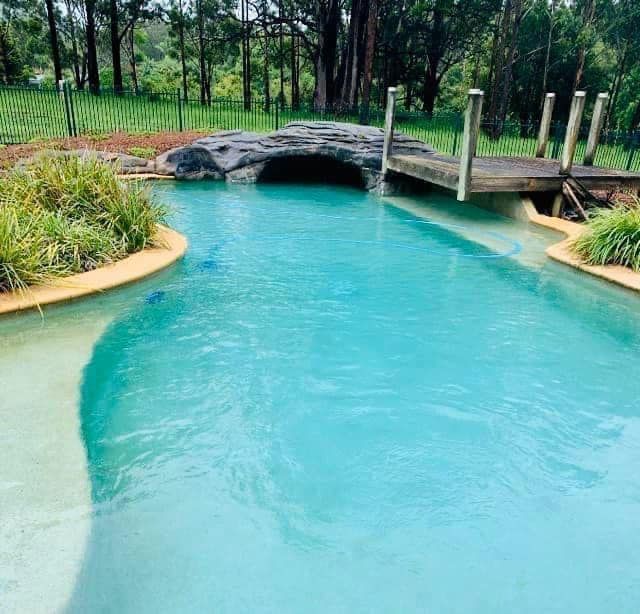 Turquoise pond with a small stone bridge and wooden dock in a landscaped garden — Cascade Pool & Spa Centre in Port Macquarie, NSW