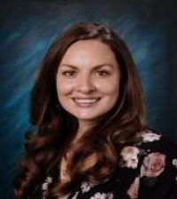 Woman in straw hat smiles, holding wine glass near a lake.