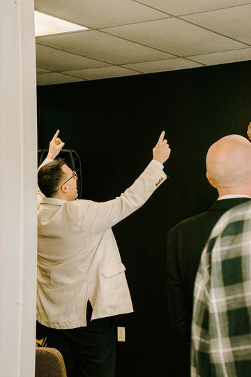 A man in a tan jacket is standing in a room with his arms in the air .