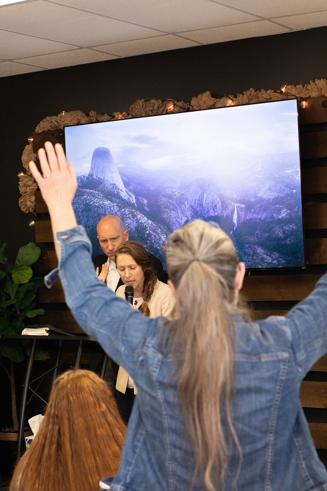 a woman is raising her hand in front of a large screen.