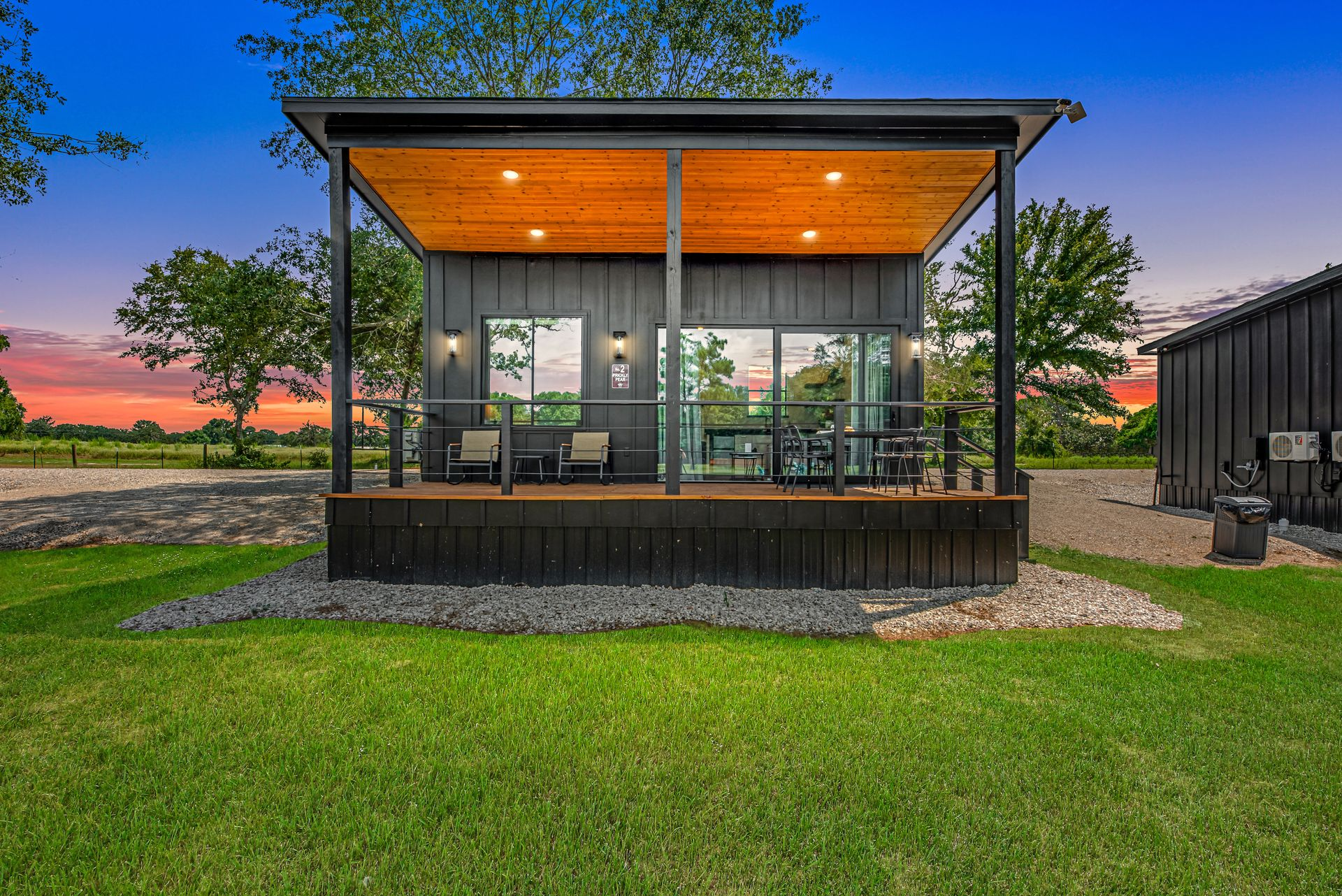 Black tiny home with a covered porch and large windows, set in a gravel area.