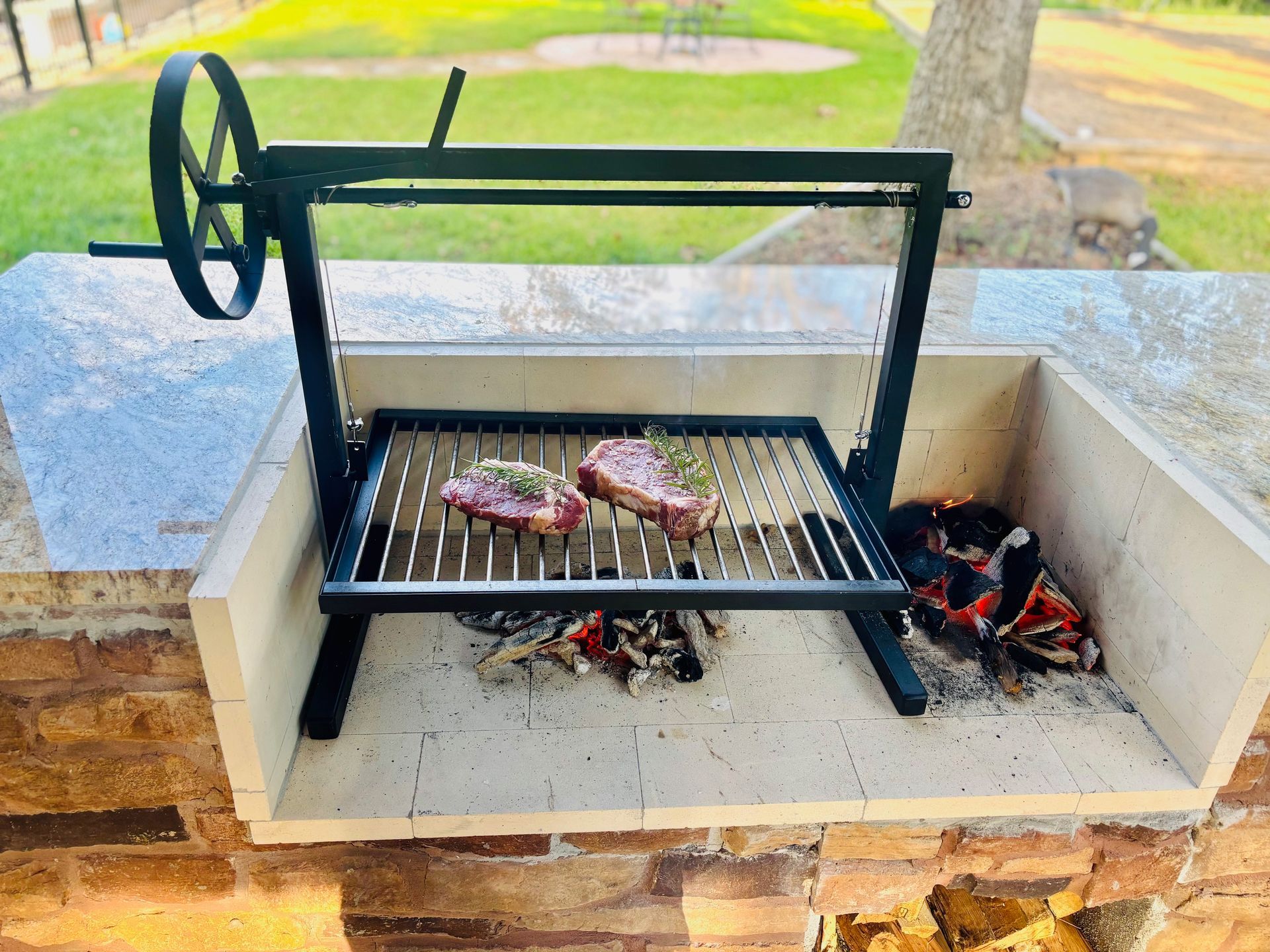 Picnic table under a covered patio with a grill and trees in the background.