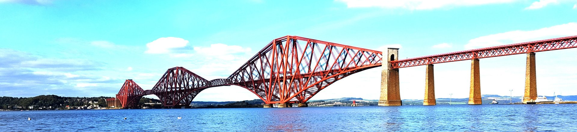 Iconic Forth Bridge spanning the Firth of Forth in Scotland, showcasing its intricate cantilever design against a scenic backdrop of water and sky.