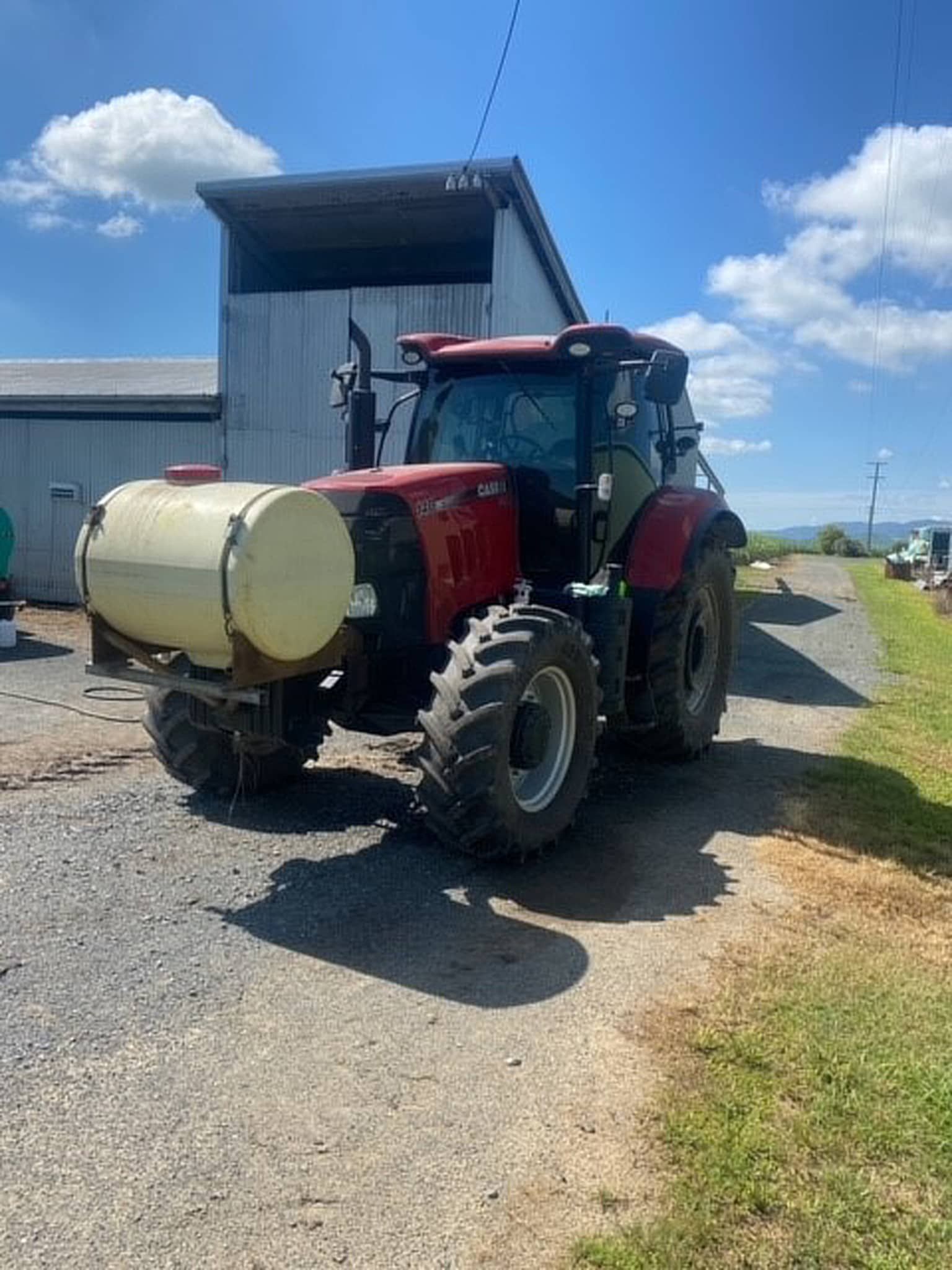 A red tractor with a tank attached to it is parked on the side of the road.