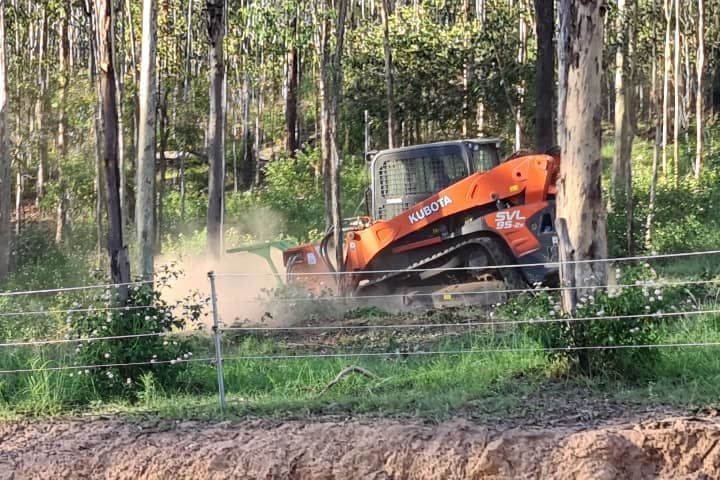 A bulldozer is driving through a forest next to a fence.