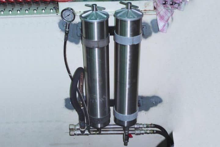 Two stainless steel cylinders with a gauge attached to them are hanging on a wall.