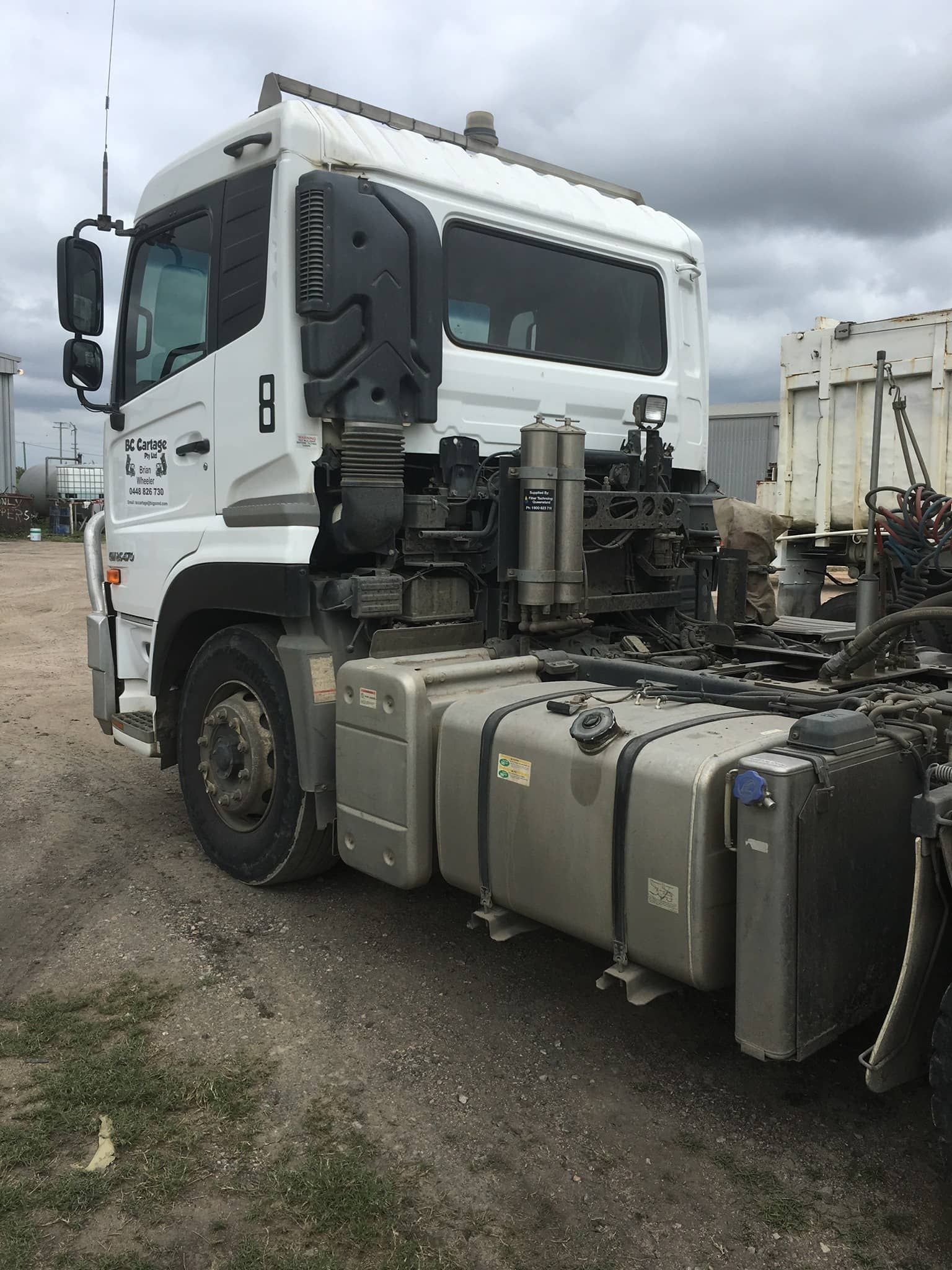 A white semi truck with a trailer attached to it is parked in a dirt lot.
