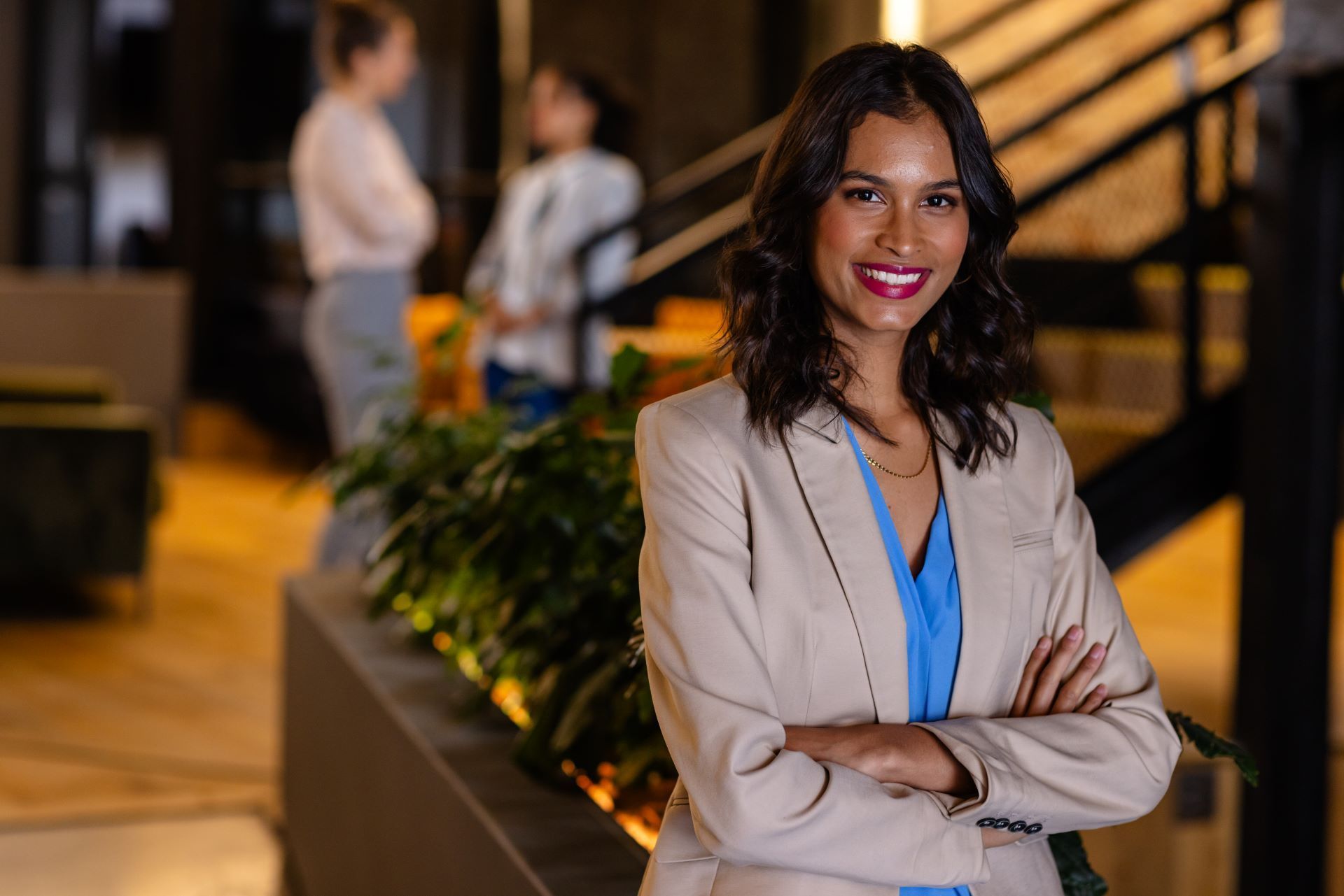 A woman in a business suit is standing with her arms crossed in an office.