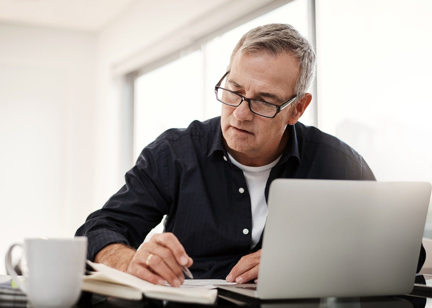 Man sitting at a table with a notepad, coffee cup, and laptop