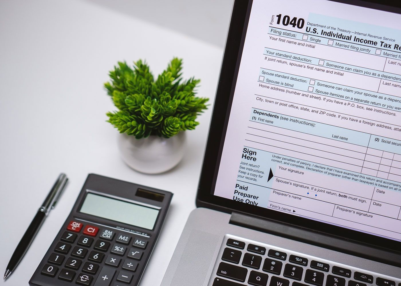 Calculator on a desk with a laptop displaying a tax form 