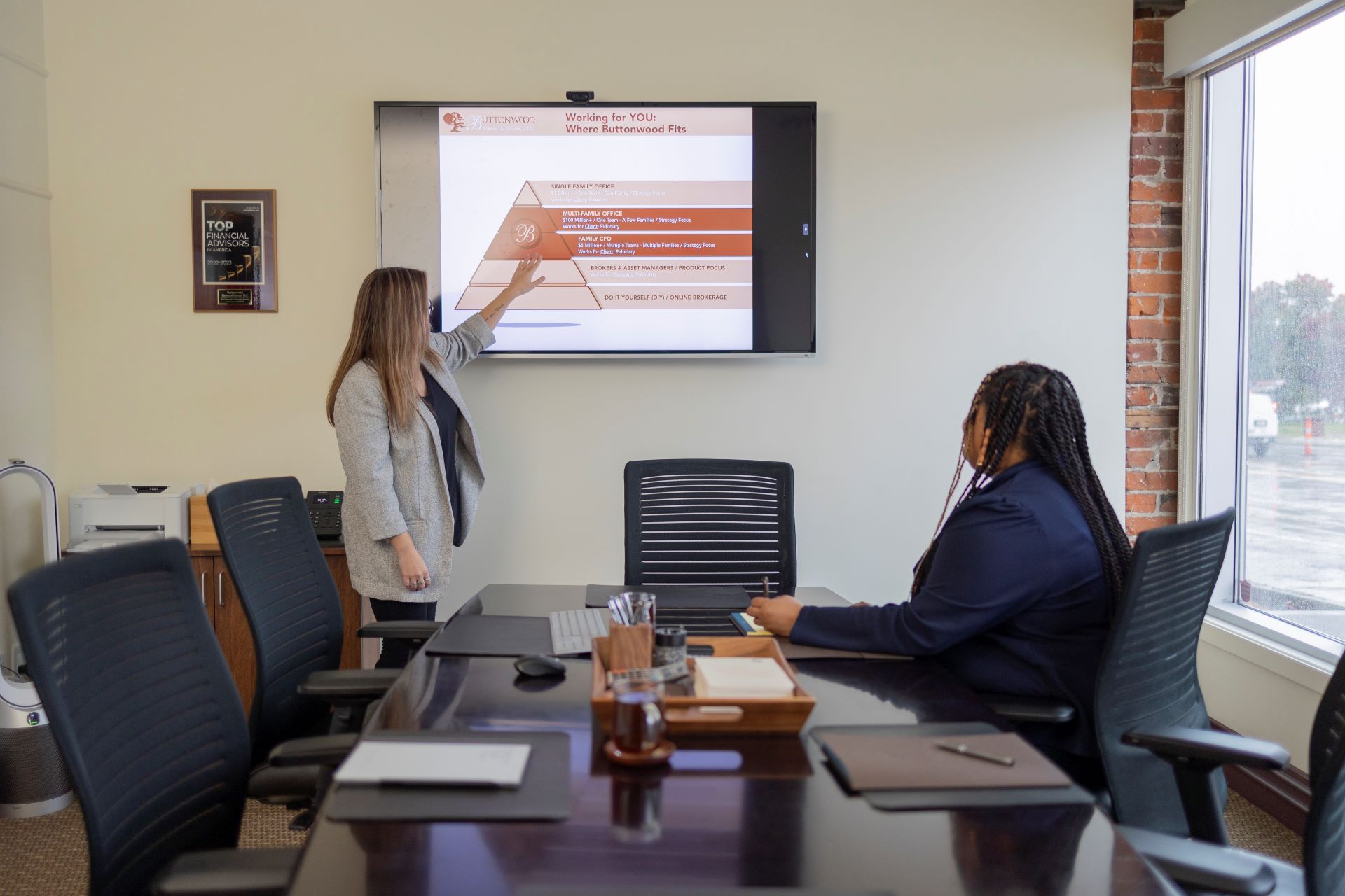 Two women are sitting at a conference table in front of a projector screen.