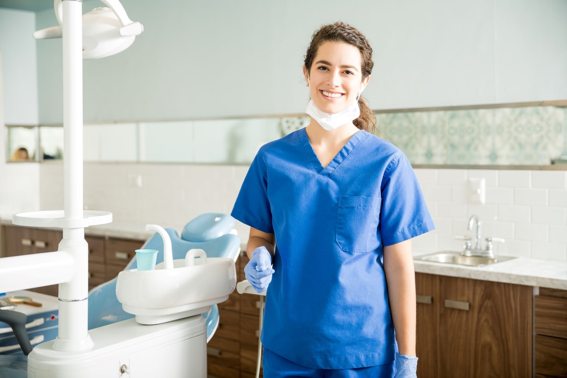 A female dentist is standing in front of a dental chair in a dental office.
