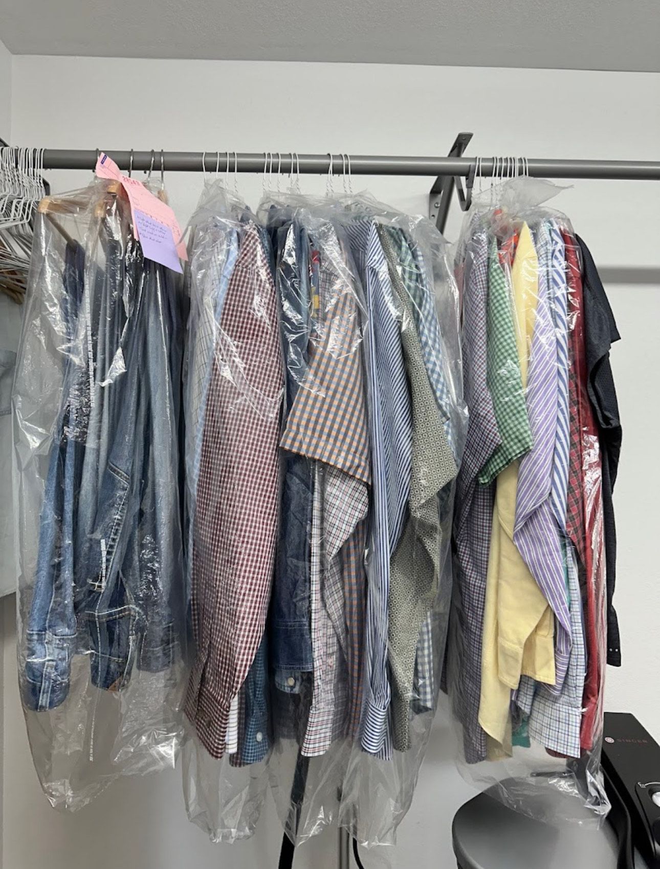 A bunch of clothes are hanging on a rack in plastic bags.