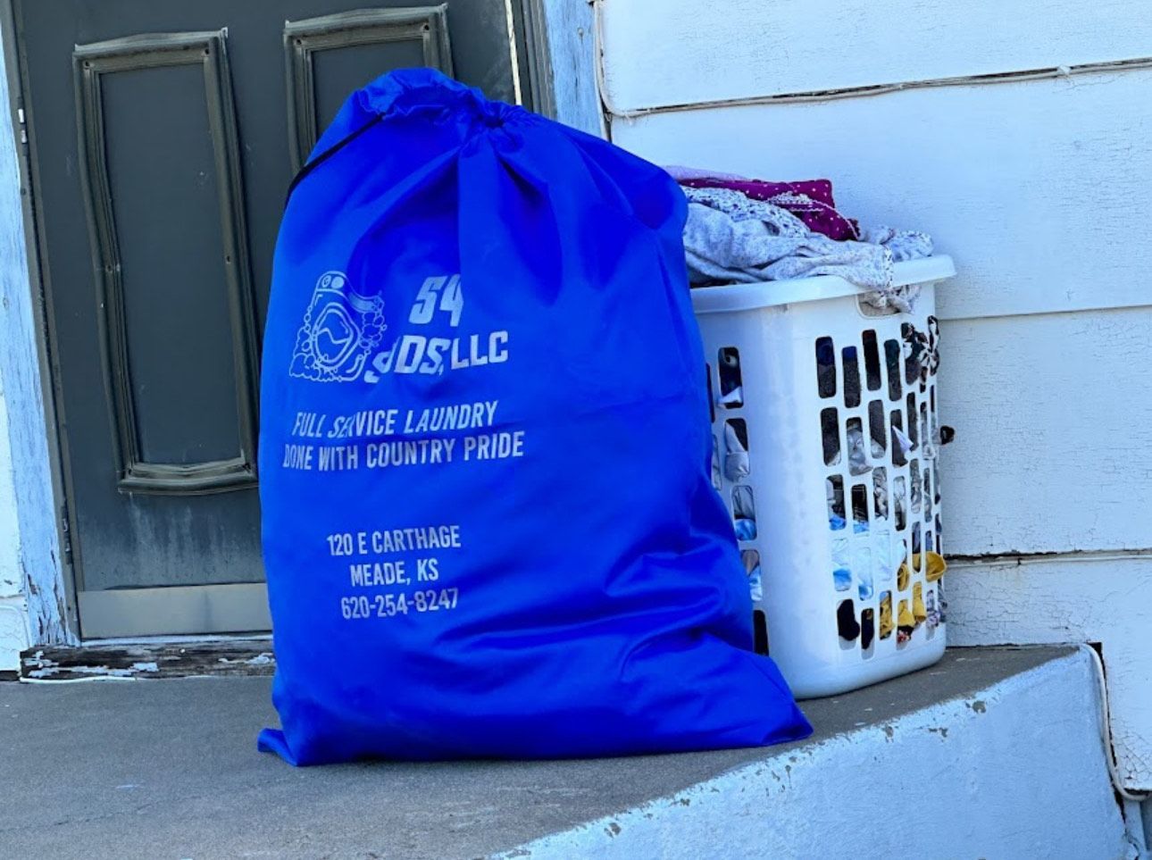 A blue laundry bag from 54 gos llc sits next to a white laundry basket