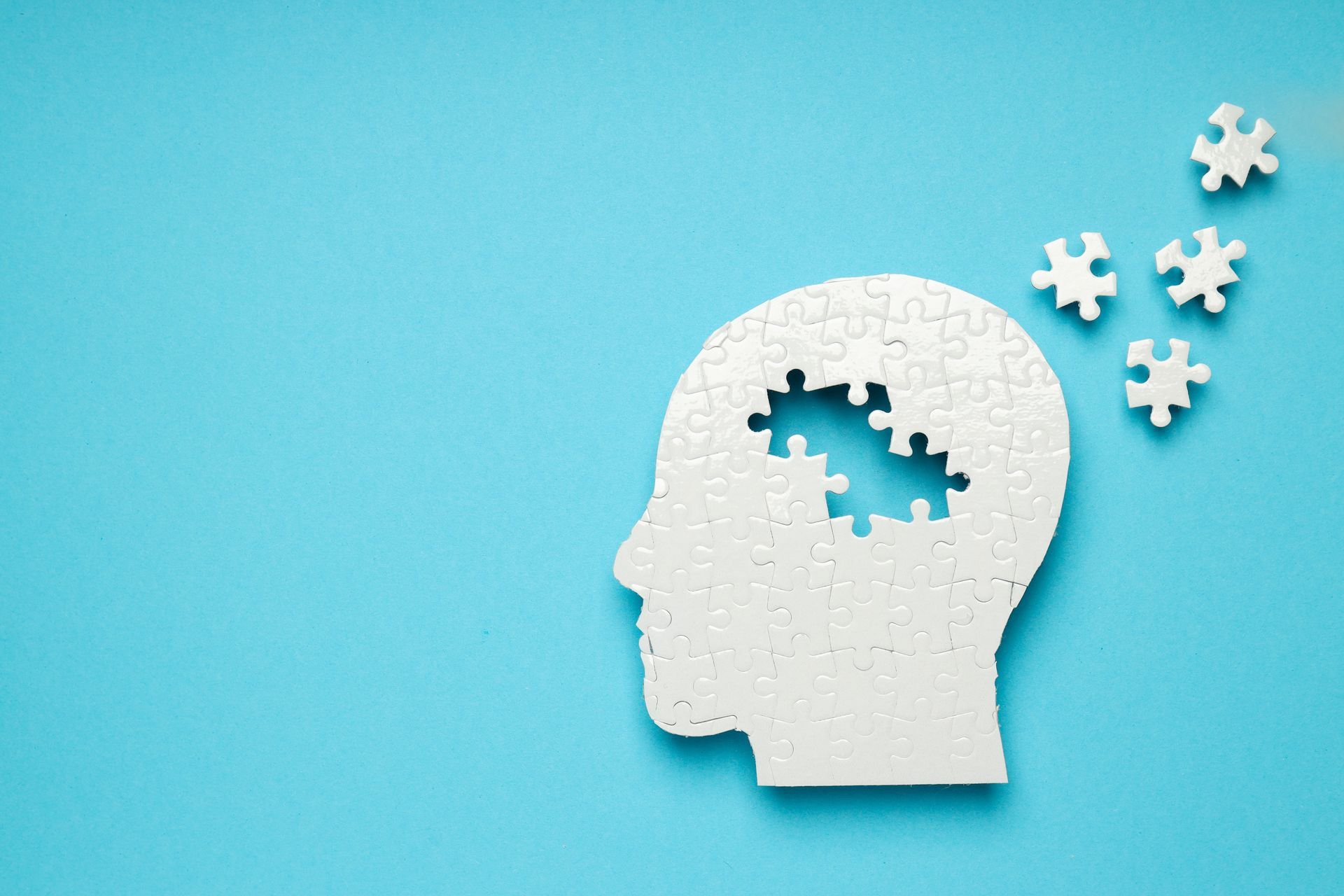 White head silhouette with missing puzzle pieces and floating puzzle pieces on a blue background