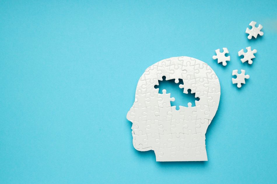 White head silhouette with missing puzzle pieces and floating puzzle pieces on a blue background