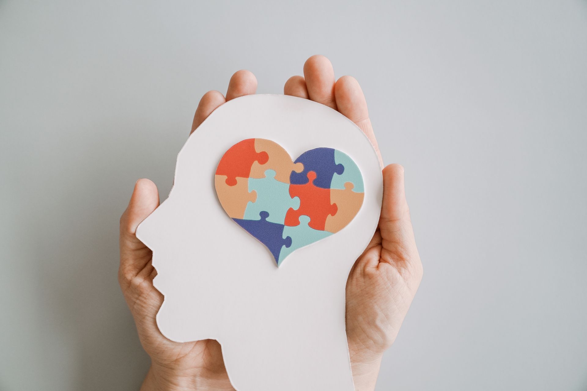 Hands holding a head silhouette with a heart-shaped multicolor puzzle inside
