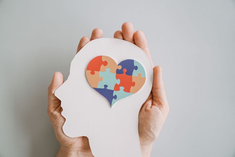 Hands holding a head silhouette with a heart-shaped multicolor puzzle inside