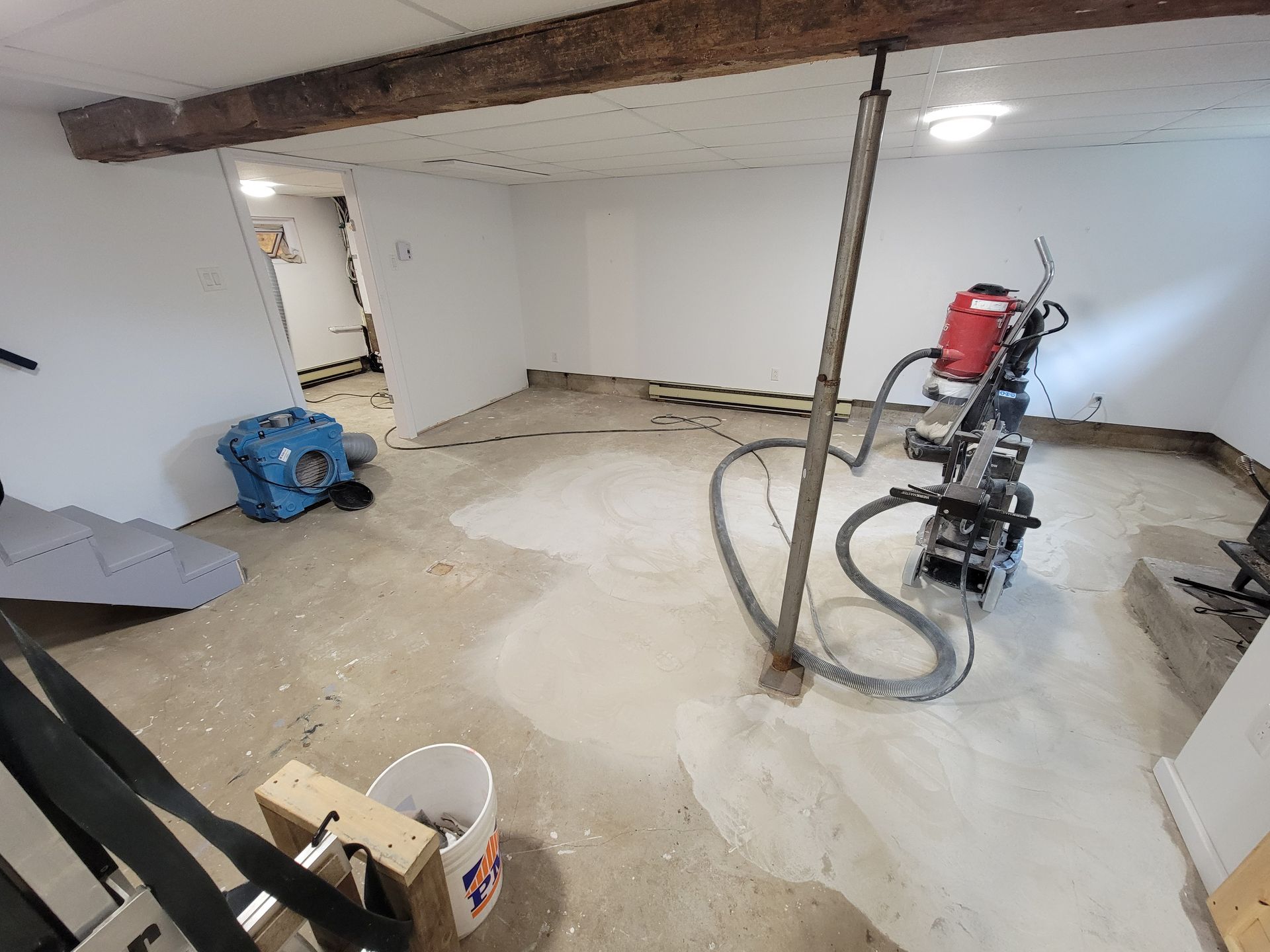 Sous-sol en rénovation avec ponceuse à plancher, plancher de béton et poutre de soutien.