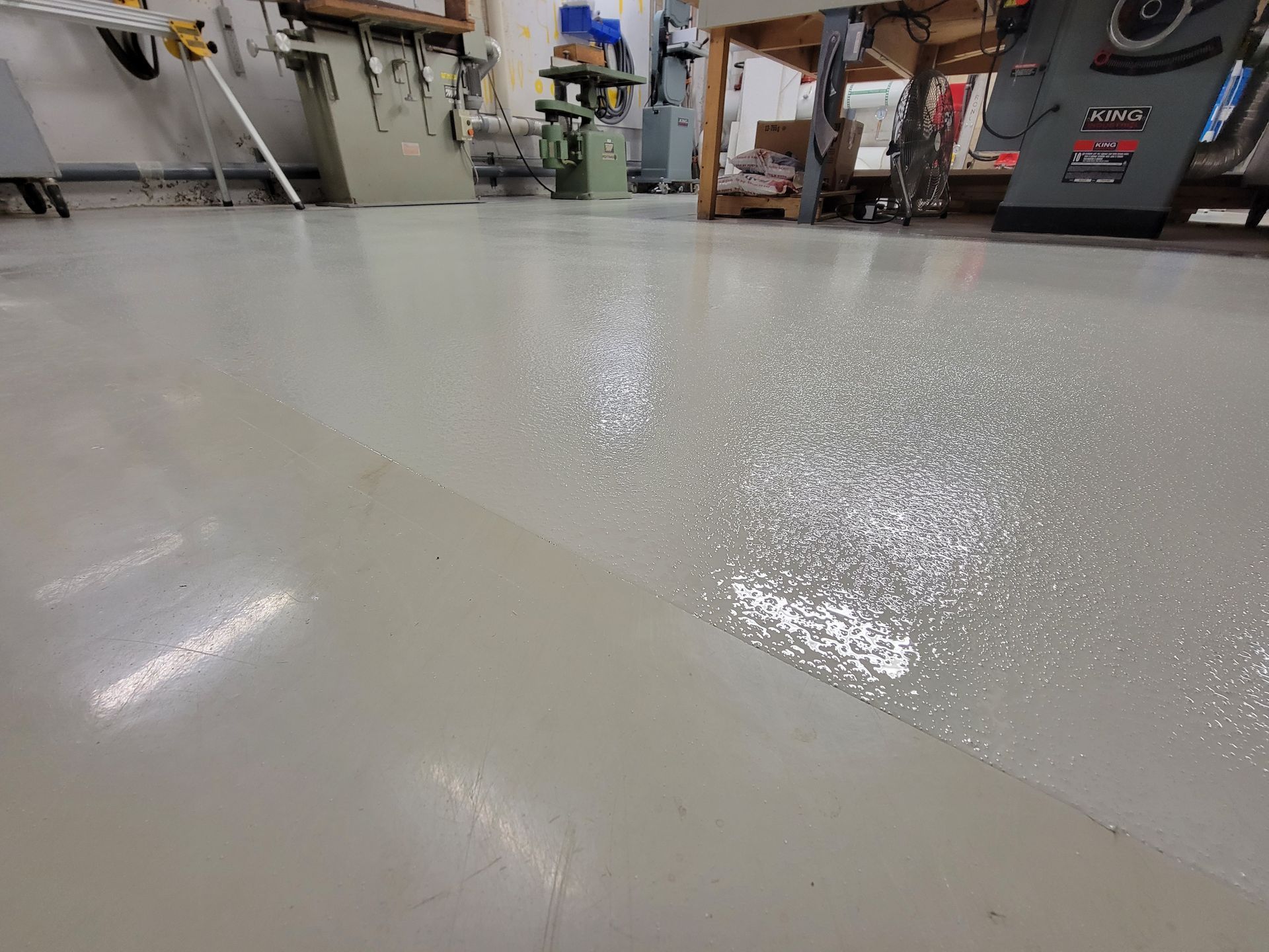 Plancher de garage en époxy gris clair avec une section fraîchement appliquée et encore brillante.