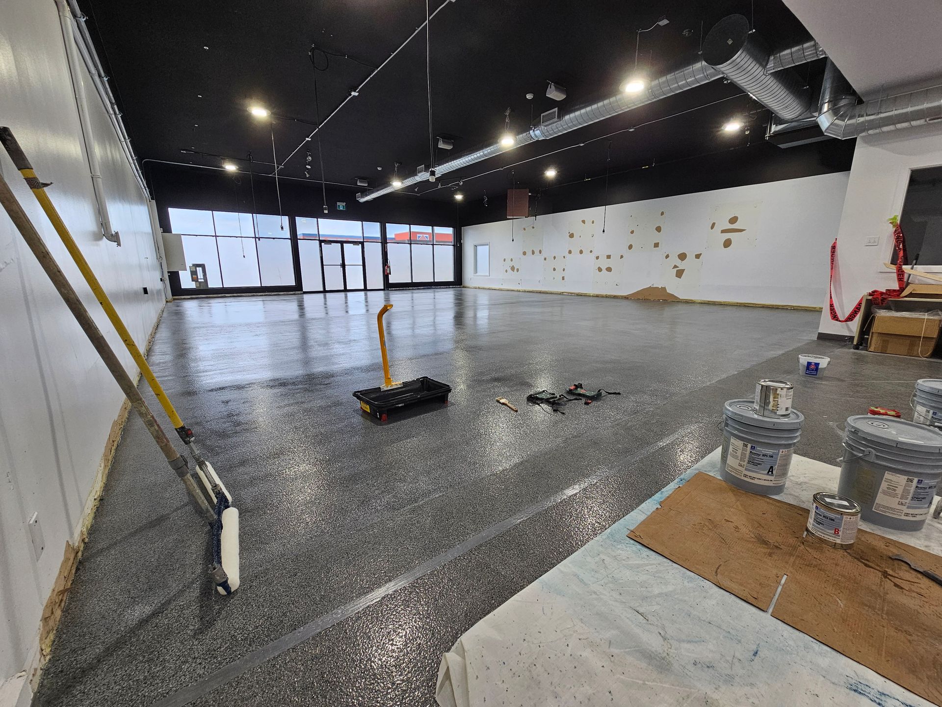 Intérieur d'un espace commercial rénové avec un sol époxy gris moucheté fraîchement coulé. Fournitures de peinture disponibles.