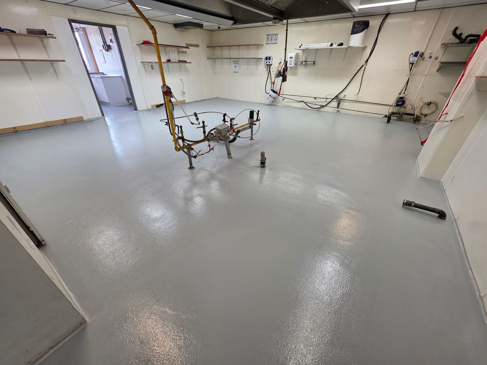 Intérieur d'un espace commercial rénové avec un sol époxy gris moucheté fraîchement coulé. Fournitures de peinture disponibles.