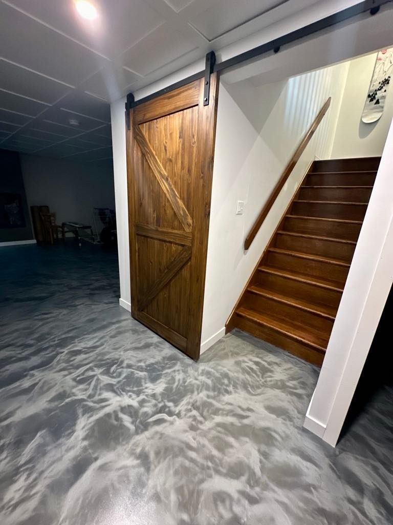 Porte de grange, escalier et sol en époxy métallisé dans une pièce. Une porte en bois est ouverte près d'un escalier.