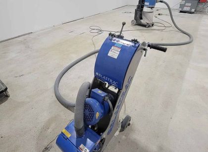 Ponceuse à sol bleue sur sol en béton, reliée à un tuyau, dans une pièce.