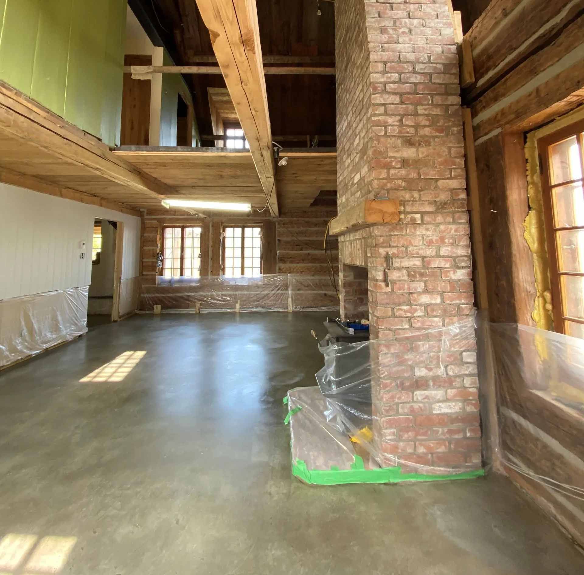 Intérieur spacieux avec cheminée en brique, poutres en bois et sol en béton.