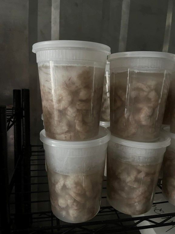 A bunch of plastic cups filled with shrimp are sitting on a shelf.
