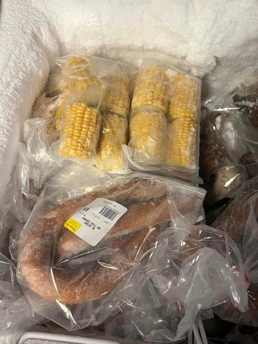 A bag of corn on the cob and a bag of sausage are in a freezer.