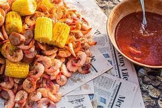 There is a bowl of soup next to a pile of shrimp and corn on the cob.