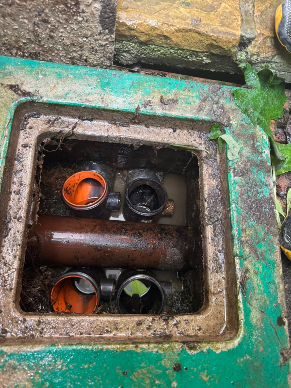 Vista dall'alto di una camera di ispezione a cielo aperto per il sistema di drenaggio, con tubature arancioni e nere e acqua stagnante.