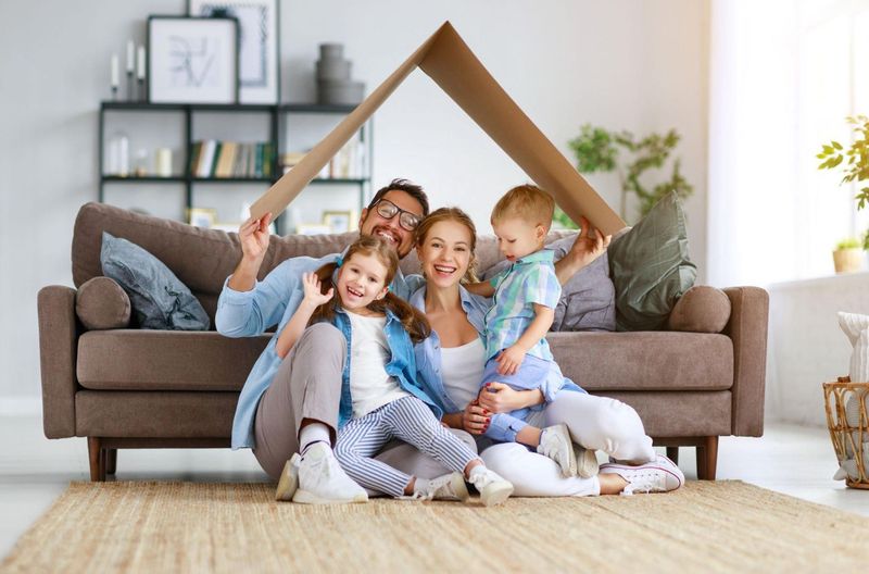 A family is sitting on a couch under a cardboard house.