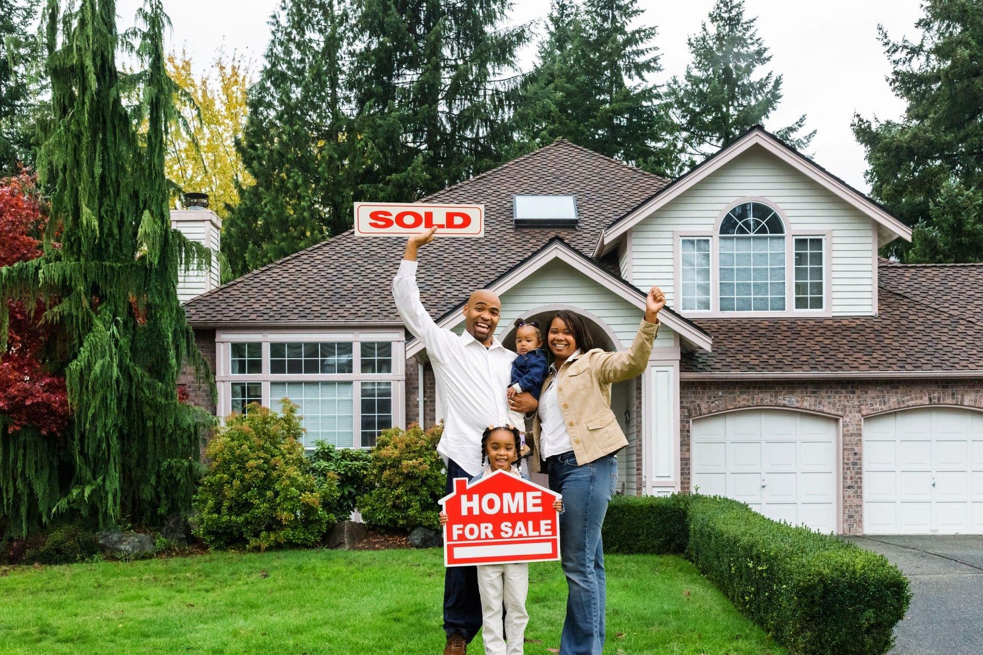 A family is standing in front of a house holding a sold sign.