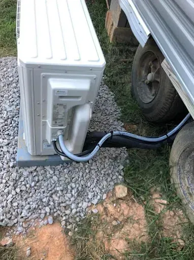 Outdoor AC unit next to a trailer; electrical and refrigerant lines run along the ground.