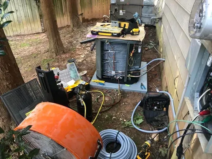 HVAC unit being serviced outdoors; tools, hoses, and equipment are scattered around the unit.