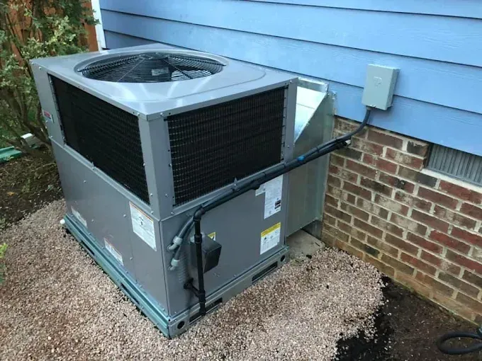 Gray HVAC unit on gravel near a brick wall and light blue siding.