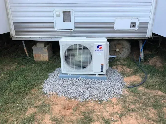 Gree mini-split air conditioner unit on gravel base near a camper.