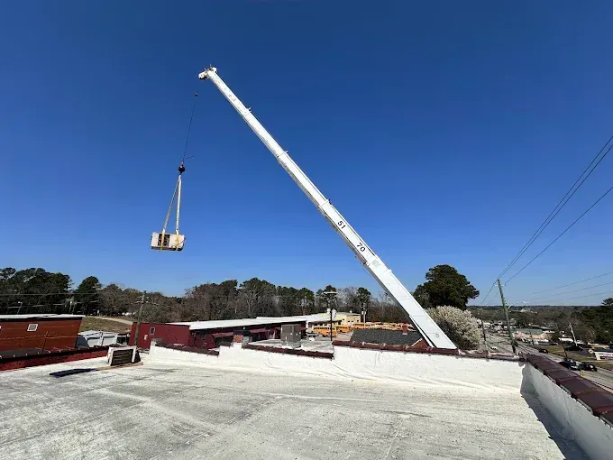 A crane lifting a rectangular object onto a flat roof on a sunny day.