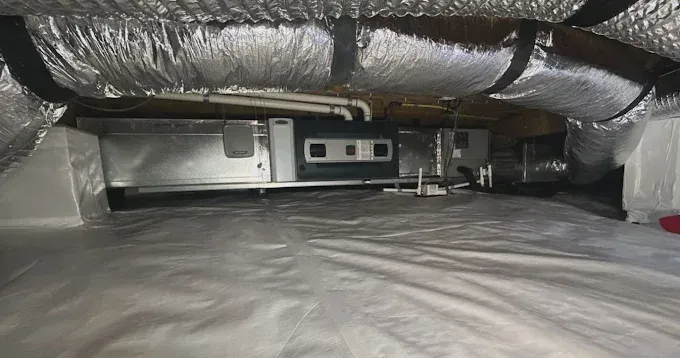 Under-house view showing HVAC equipment and ductwork, with insulation on ceiling and vapor barrier on the ground.