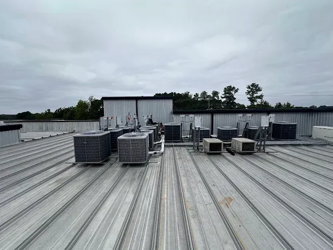 Rooftop with several air conditioning units on a corrugated metal surface under a cloudy sky.