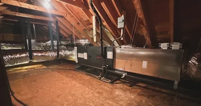 HVAC system in an attic. Ductwork, wooden beams, insulation, and electrical components.
