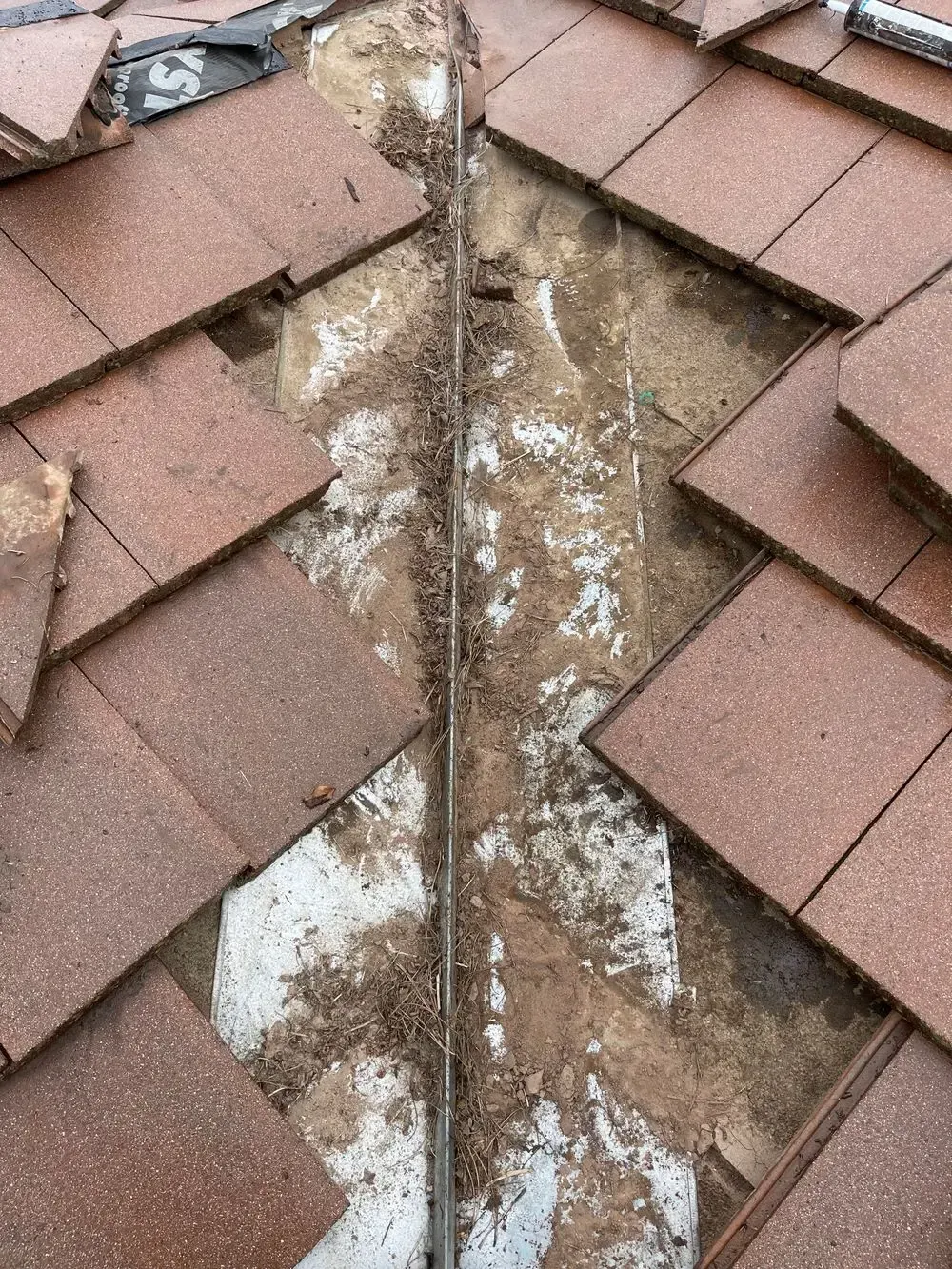 A close up of a roof with tiles and a metal pipe.