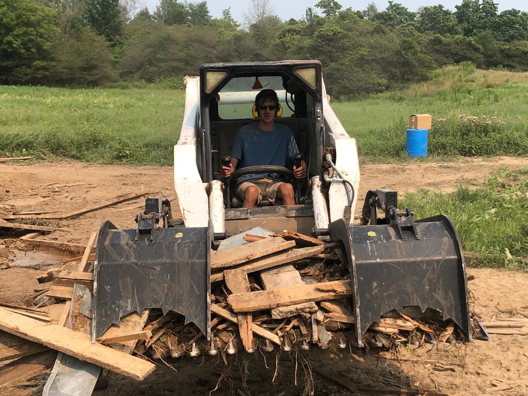 A man is sitting in a bulldozer filled with wood.