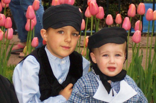 Two young boys wearing black hats are posing for a picture in front of pink tulips