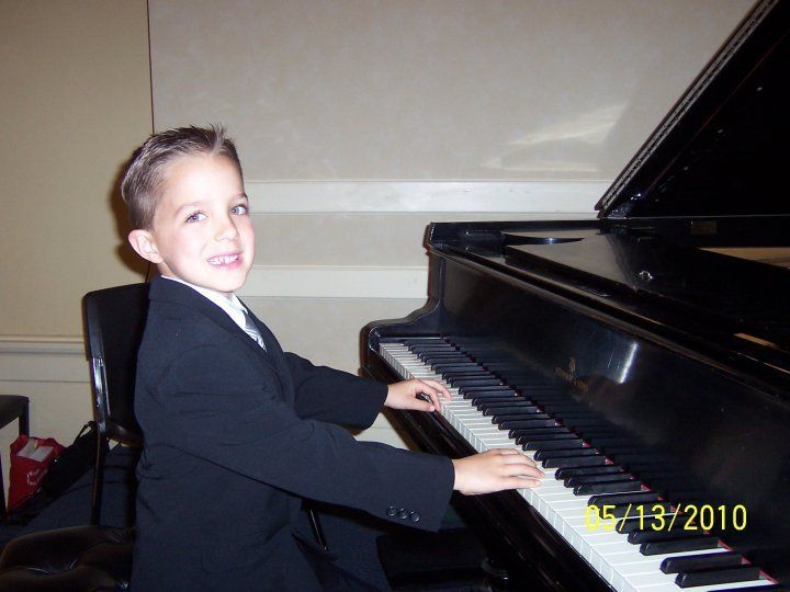 A young boy in a suit is playing a piano