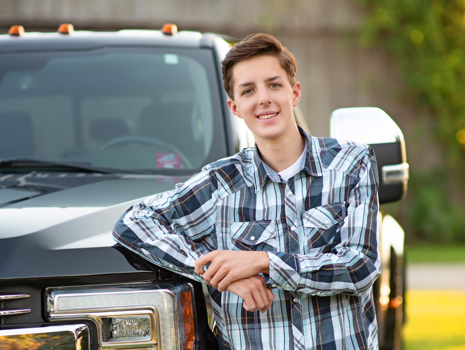 A young man is leaning on the hood of a truck.