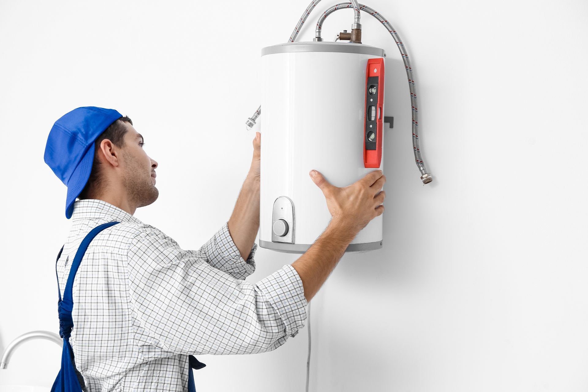 Plumber in blue cap installing a white water heater on a white wall.